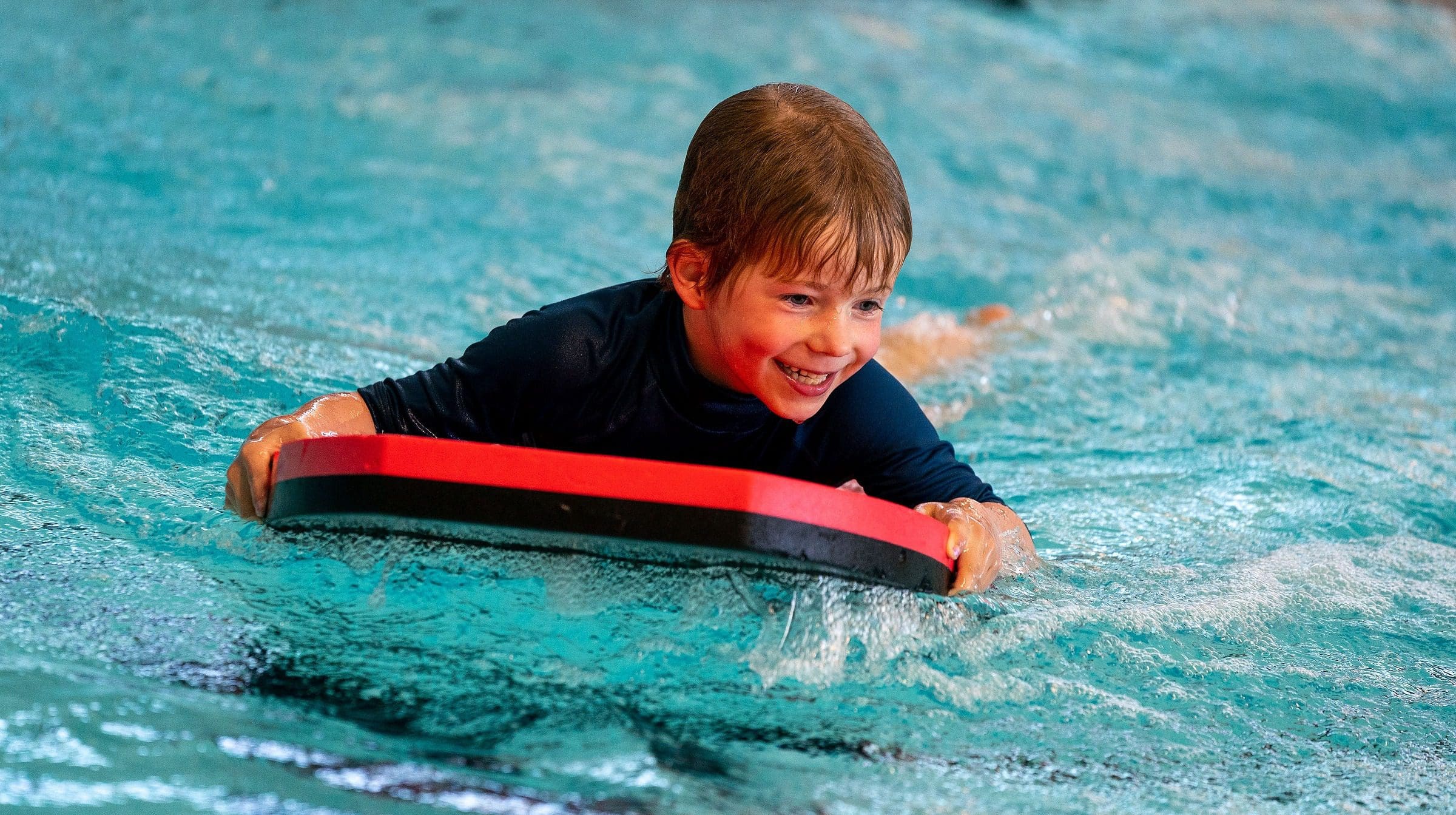 lachende jongen op bord in zwembad