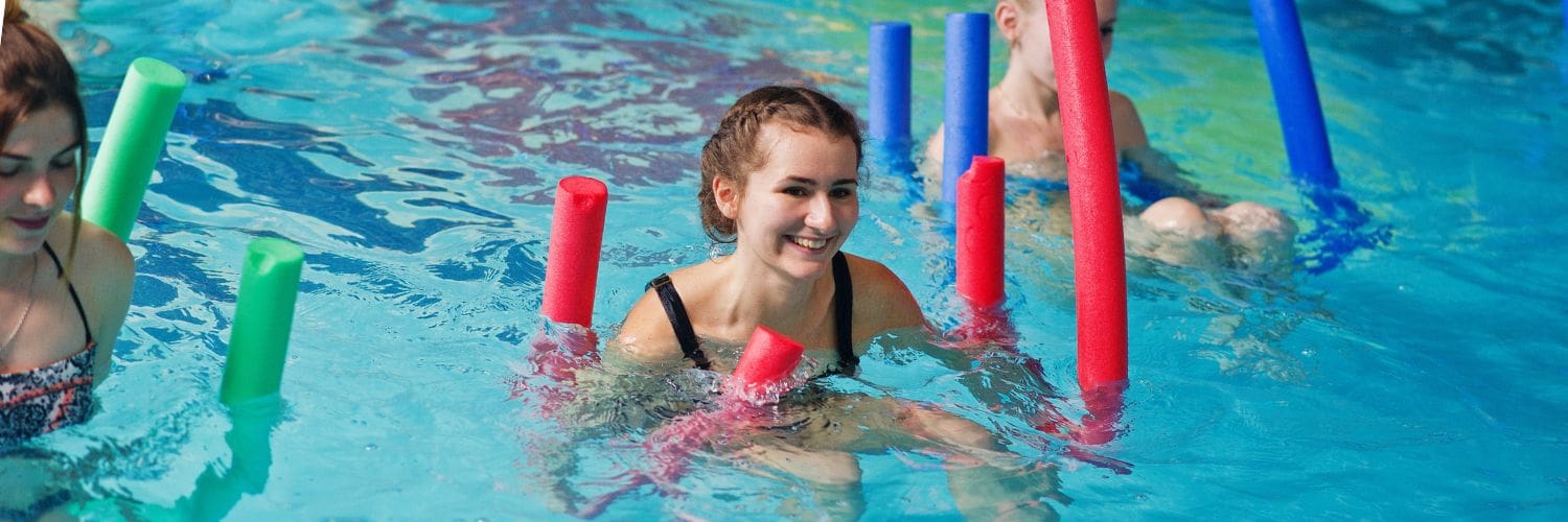 Groepje sporters in het zwembad die drijven met behulp van Pool Noodles