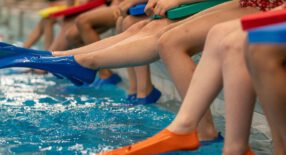 Benen van kinderen, zittend op zwembadrand met zwemflippers aan
