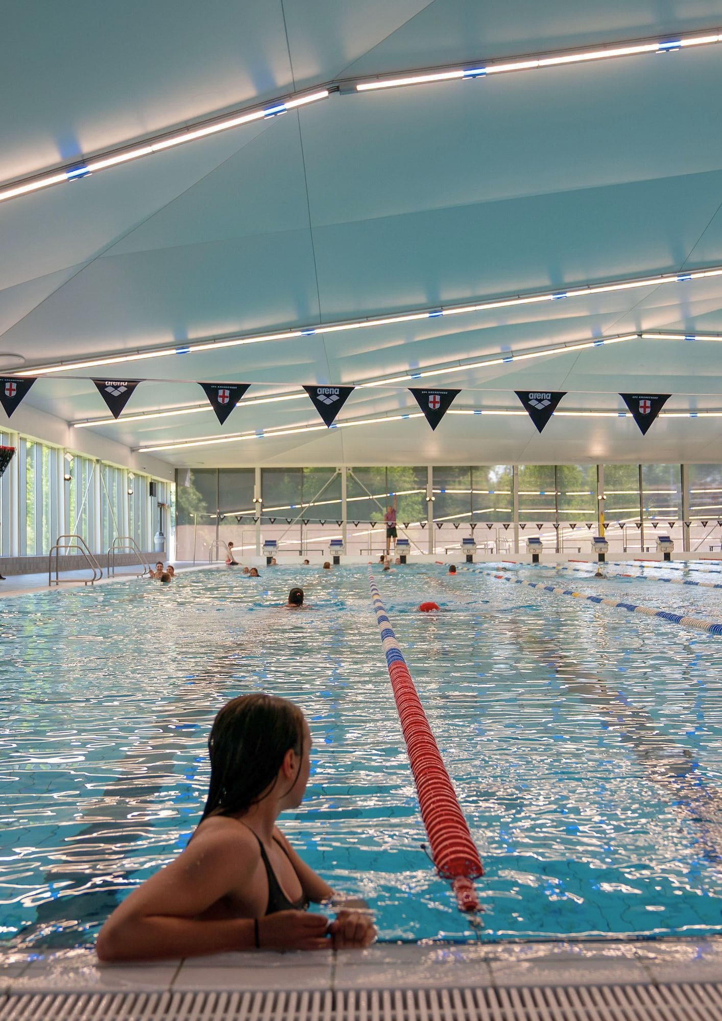 Vrouw leunt op badrand van het 50 meter bad in Amerena terwijl ze naar de andere zwemmers kijkt