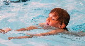 Jongetje met rossig haar zwemt schoolslag