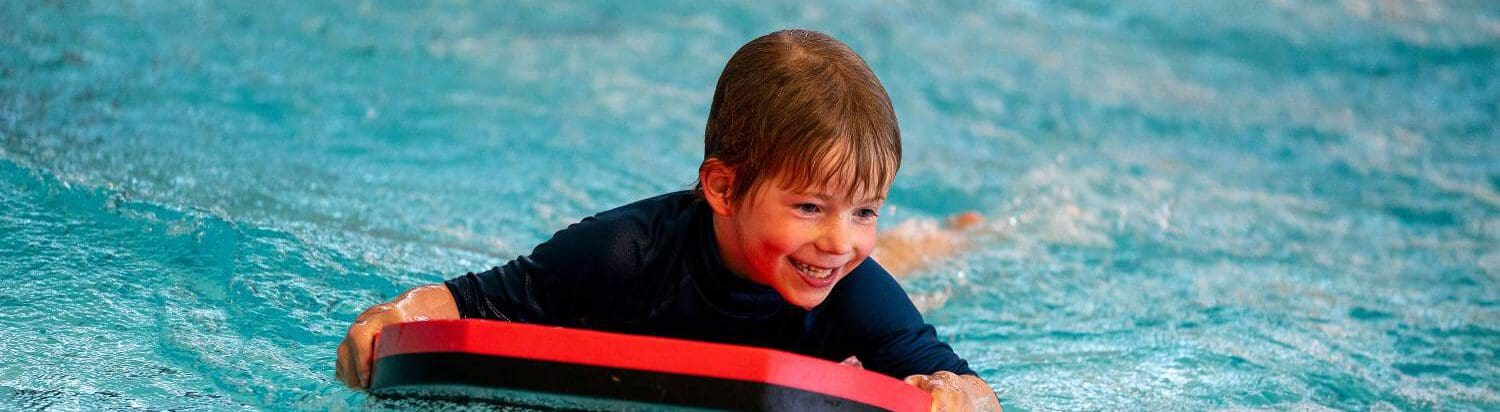 jongetje heeft plezier op een rood foambord in het zwembad