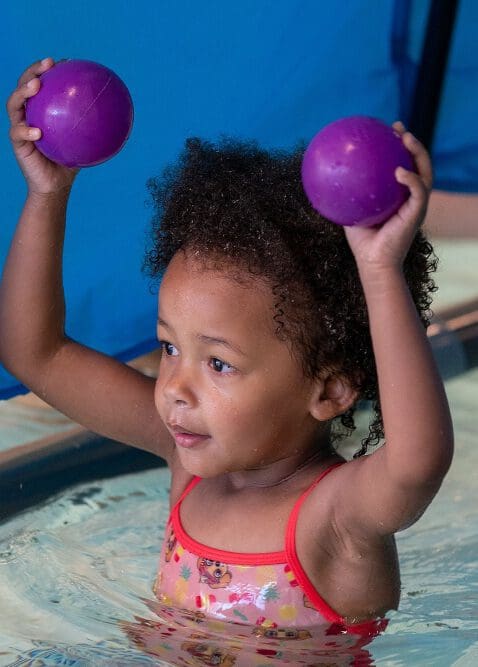 meisje speelt met twee paarse balletjes in het zwembad