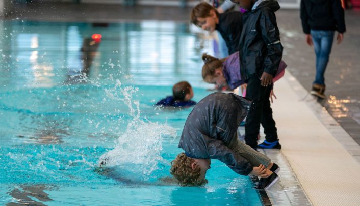 Kinderen duiken met kleding aan het zwembad in voor het halen van hun C zwemdiploma