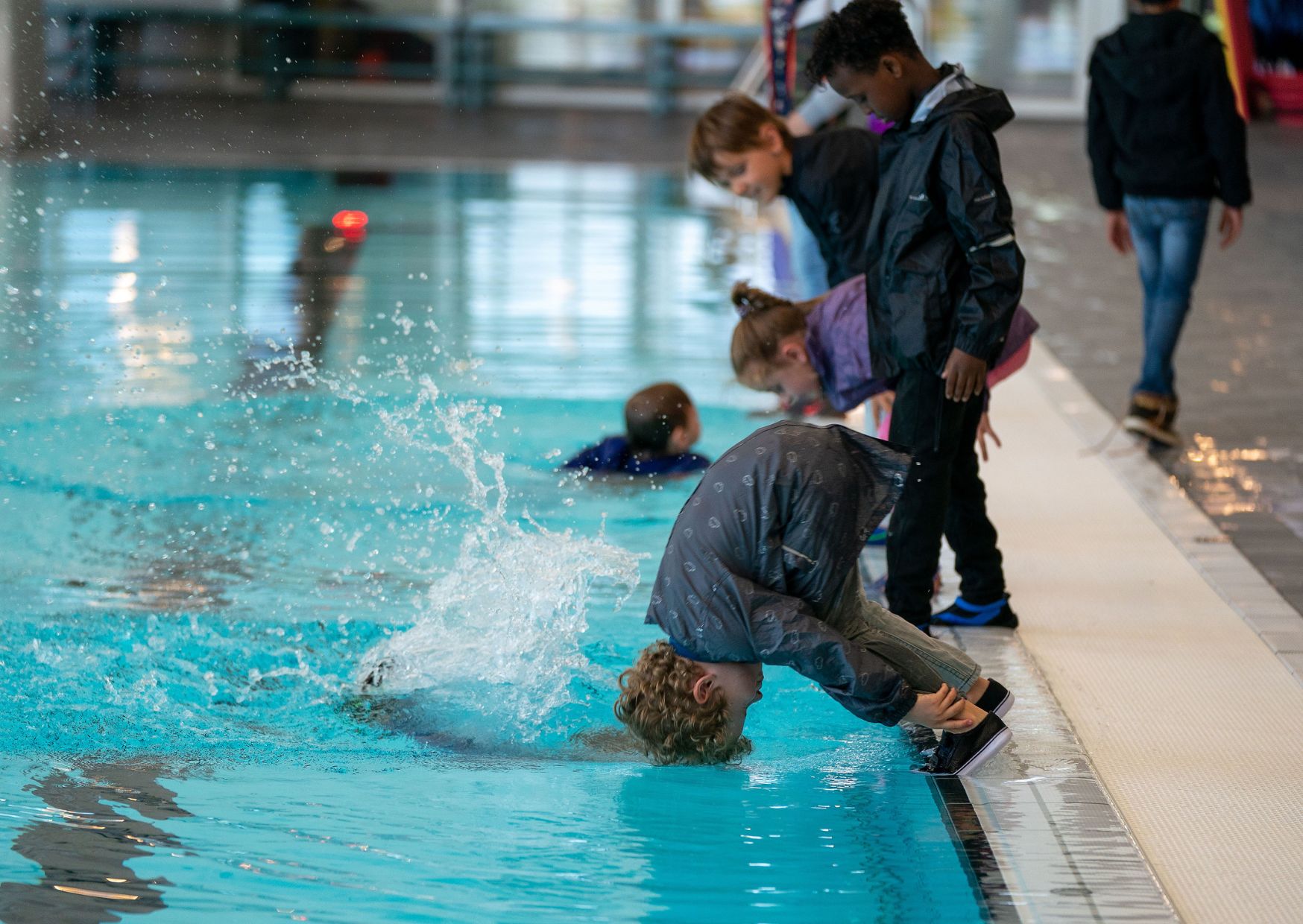 Kinderen duiken met kleding aan het zwembad in voor het halen van hun C zwemdiploma