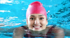 lachende vrouw met rode badmuts zwemt schoolslag