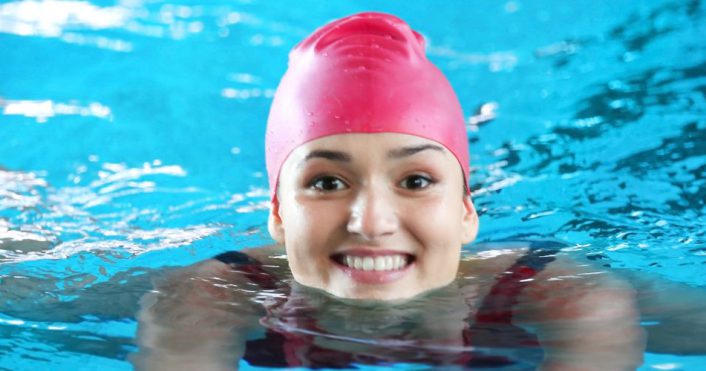 lachende vrouw met rode badmuts zwemt schoolslag