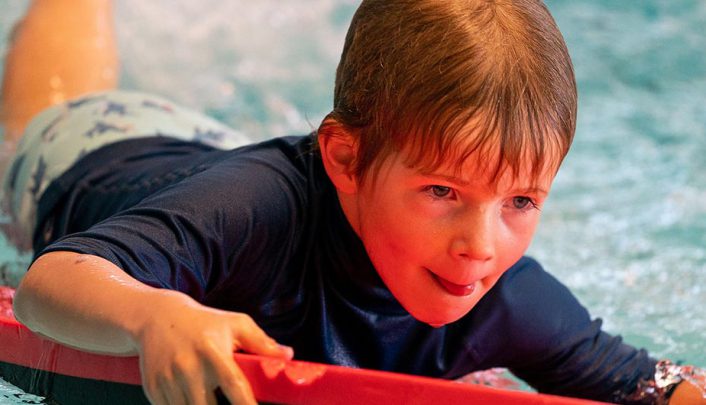 jongetje heeft plezier op een rood foambord in het zwembad