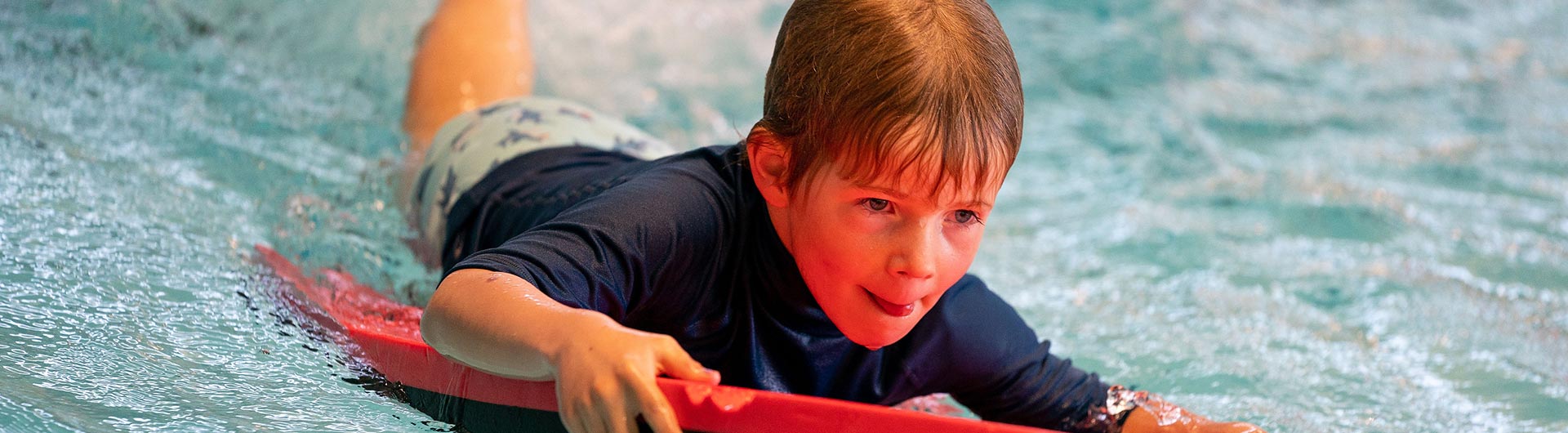 jongetje heeft plezier op een rood foambord in het zwembad
